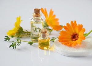 Two small glass bottles with bright orange flowers laid behind them