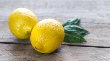 Two ripe lemons on top of basil leaves laid on a wood deck