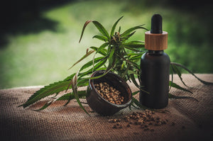 Oil dropper bottle with untrimmed cannabis leaf and cannabis seeds beside it in a small bowl