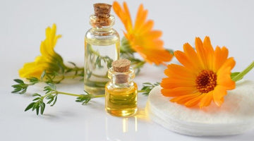 Two small glass bottles with bright orange flowers laid behind them